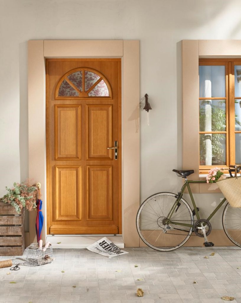 Porte d'entrée en bois marron clair à côté de laquelle repose un vélo