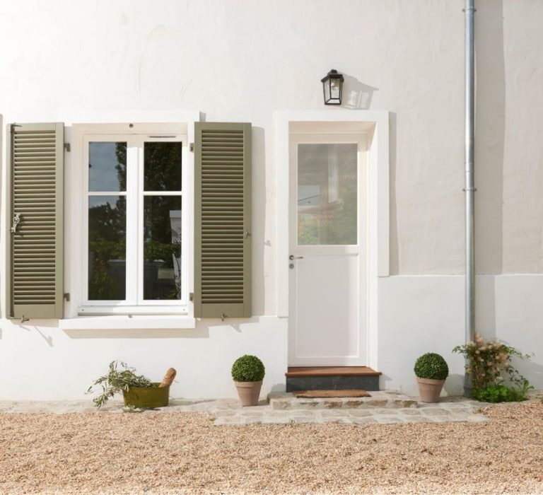 Extérieur d'une maison blanche avec une fenêtre aux volets vert olive