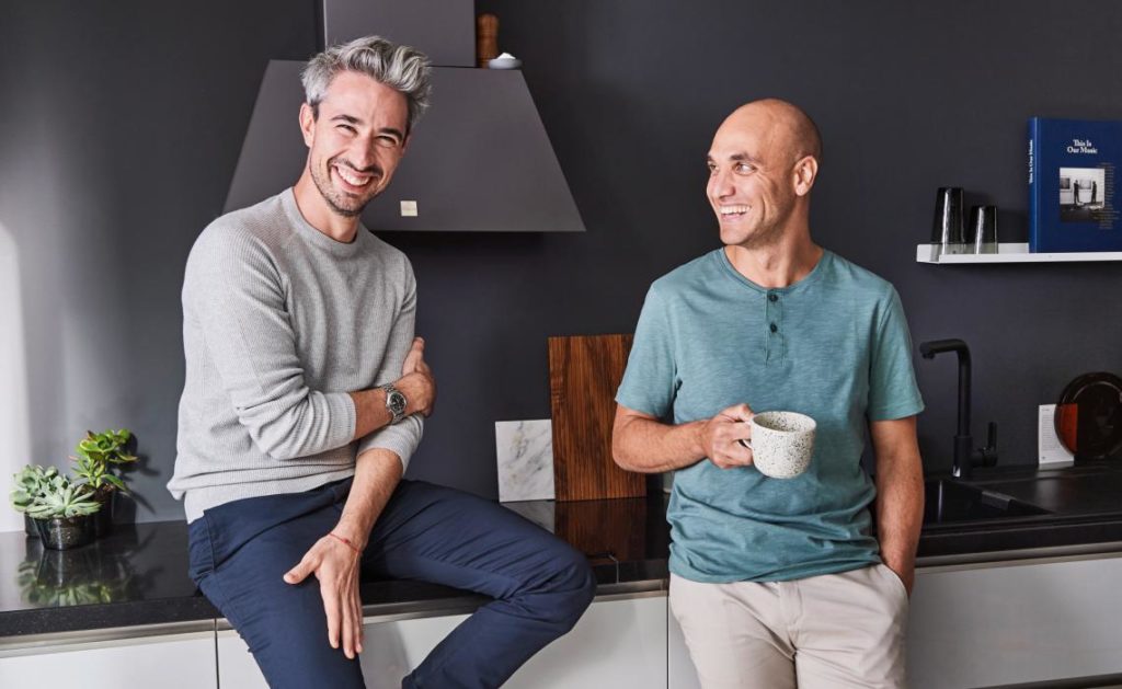 Deux hommes heureux adossés au plan de travail de leur cuisine